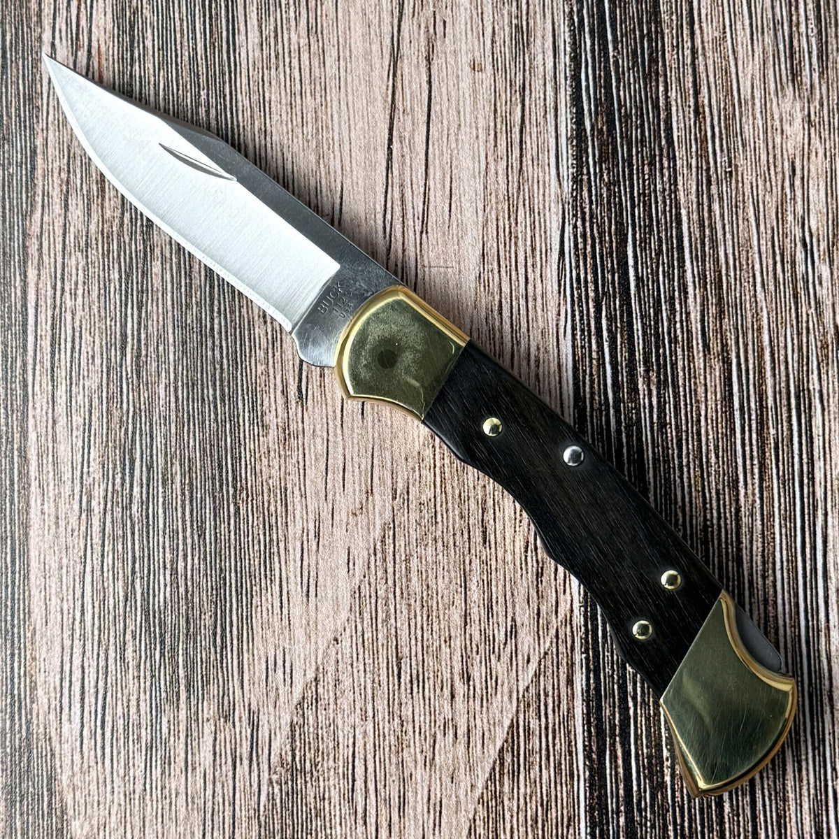 Buck 112 Ranger with clip-point blade open, ebony handle, and brass bolsters on a wood surface